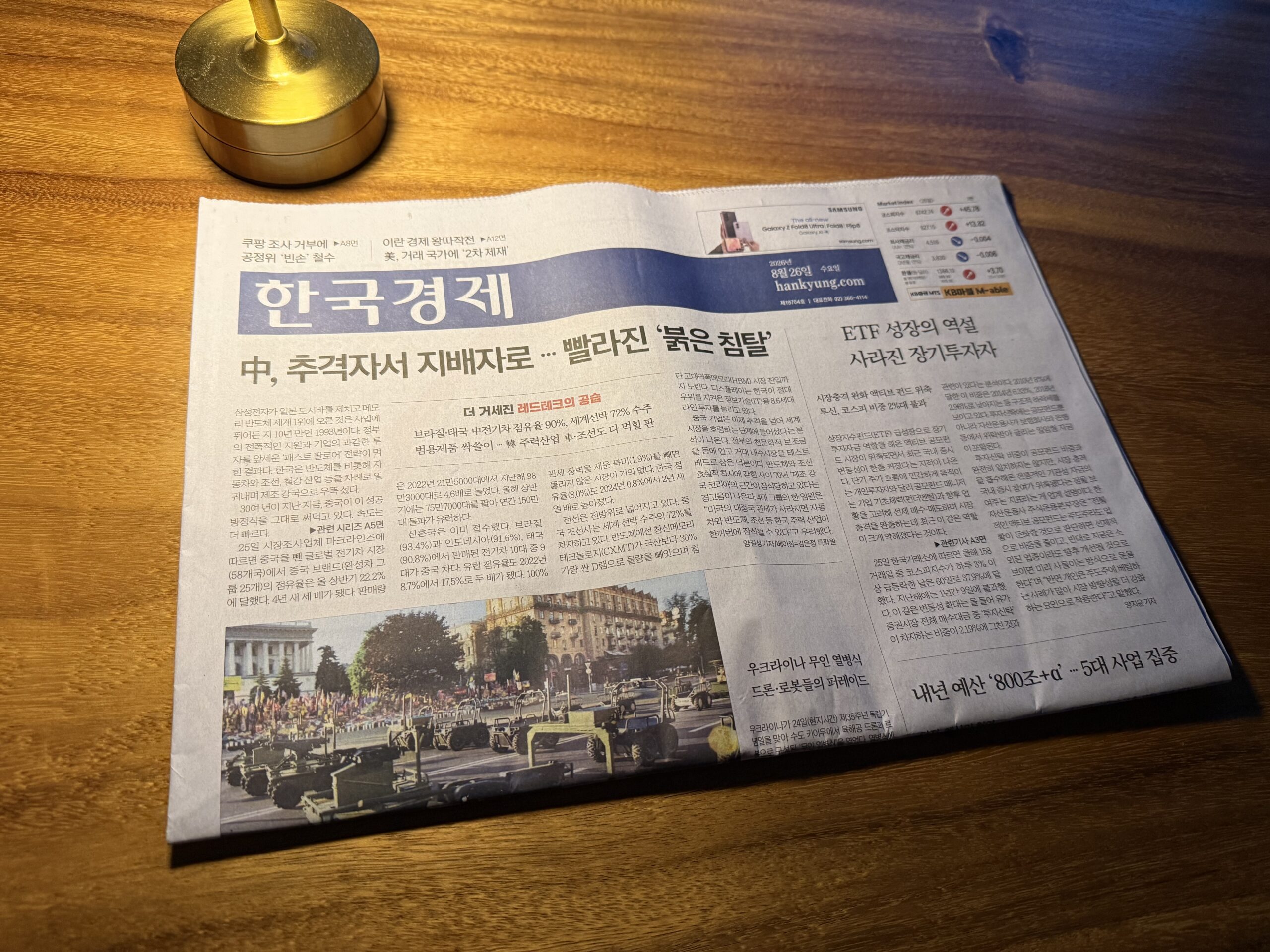 어두운 조명 아래 원목 식탁에 펼쳐 둔 한국경제신문 1면, 위쪽에 놋쇠 촛대가 놓여 있다. 머리기사는 '中, 추격자서 지배자로 … 빨라진 붉은 침탈'이고 아래에는 광장에서 군용 차량이 줄지어 지나가는 열병식 사진이 실려 있다.