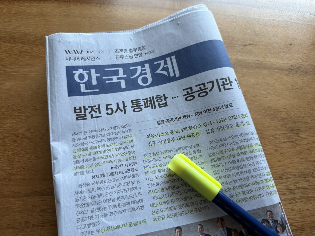 나무 책상 위 한국경제신문 1면과 노란 형광펜. 머리기사는 '발전 5사 통폐합 … 공공기관'이고 왼쪽 문단과 부제 여러 줄에 형광펜이 그어져 있다.